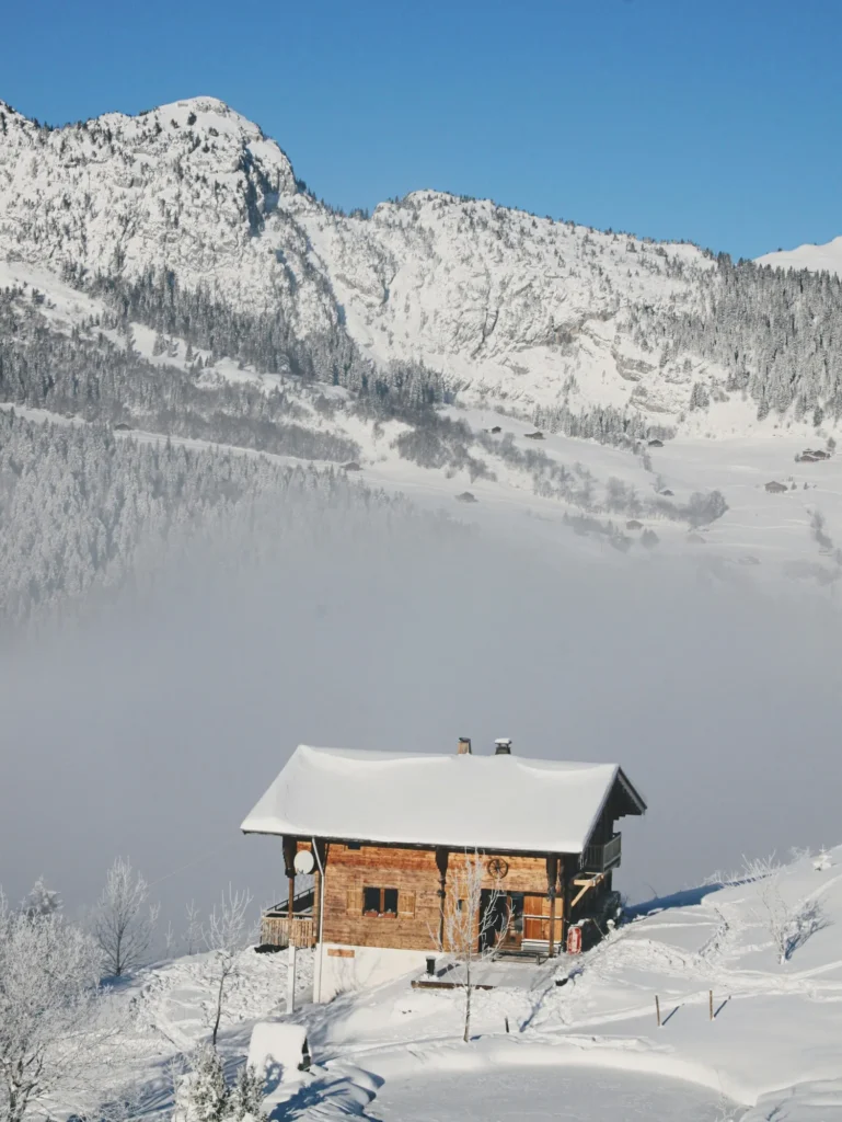 Chalet traditionnel en bois sous la neige, au-dessus d’une mer de nuages